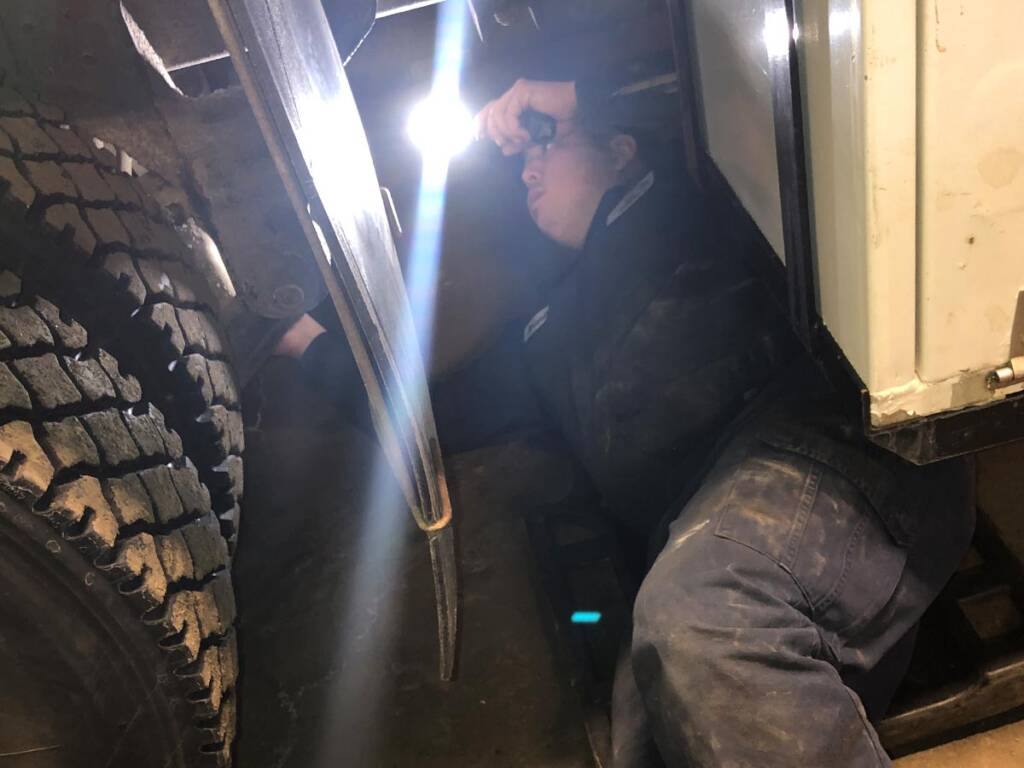 mechanic checking electrical wires on the underside of a truck