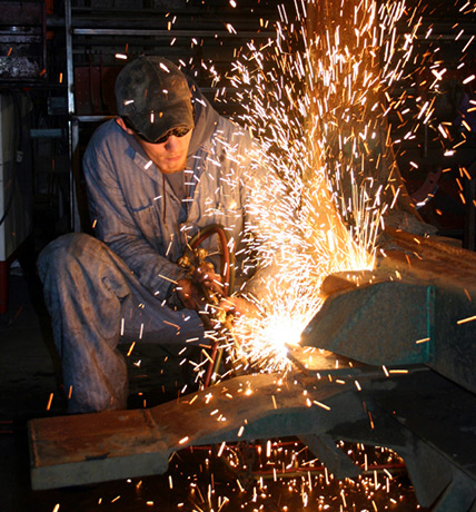 a welder sitting down welding a piece of metal, welding fire coming out infront oh him
